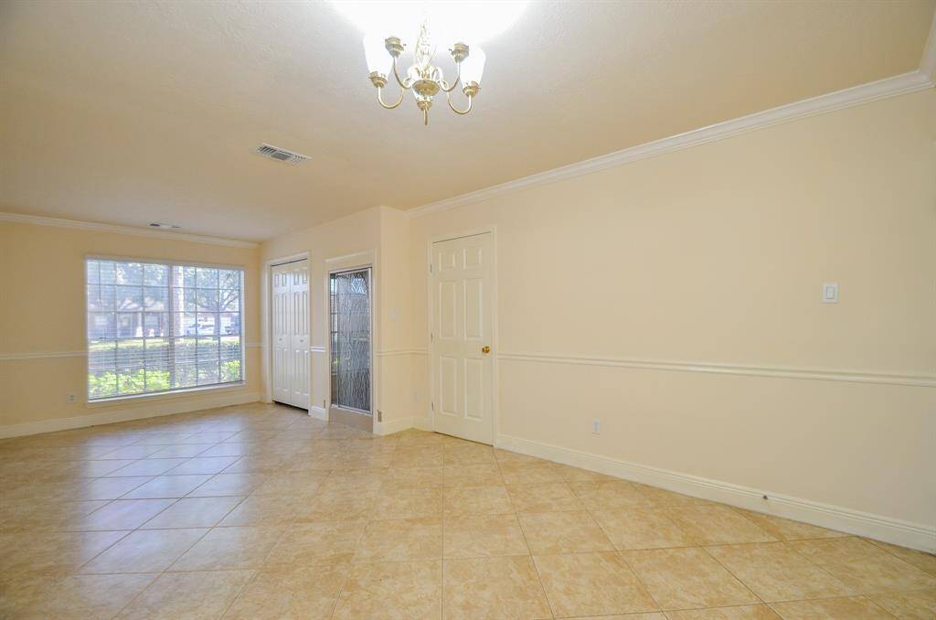 Another view of the bright, spacious bedroom on first floor with large windows, tiled floors, and a chandelier. The neutral walls and crown molding create a clean, inviting atmosphere.
