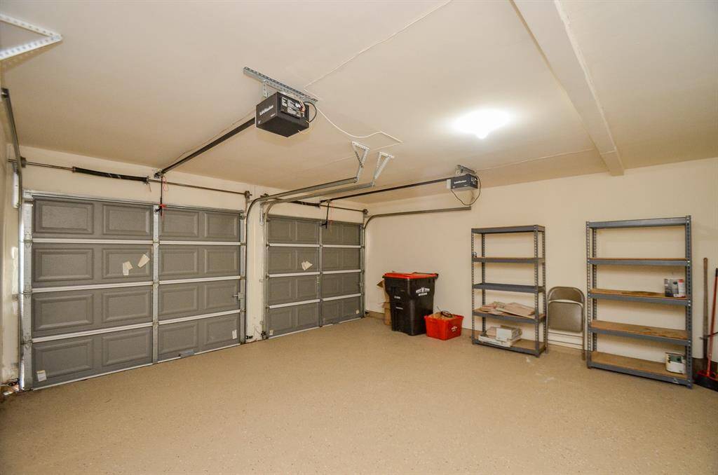 Spacious two-car garage with clean walls and floors, equipped with shelving for storage and overhead lighting.
