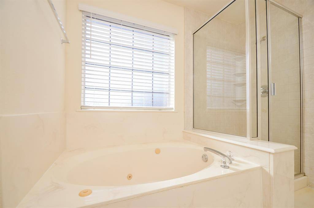 This Primary bathroom features a cozy corner bathtub with a large window above, offering natural light. Adjacent is a spacious glass-enclosed shower, all in a clean, neutral design.