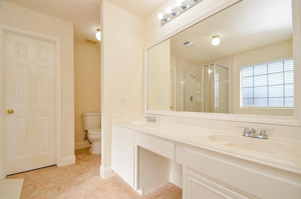 Another view of the spacious Primary bathroom with a large mirror, dual sinks, and a glass-enclosed shower. Features a separate toilet area and bright natural lighting from the window.