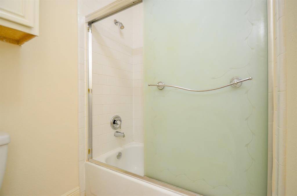 This photo shows another view of the second full bathroom with a clean, modern bathtub and a frosted glass sliding door. The white tile surround and light-colored walls create a bright and inviting space.
