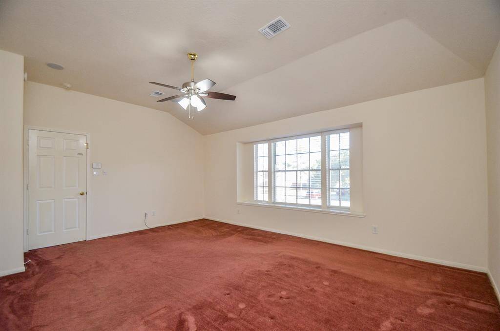 Bright Primary bedroom on second floor with vaulted ceilings, featuring a large window that offers plenty of natural light. Includes a ceiling fan and red carpet.