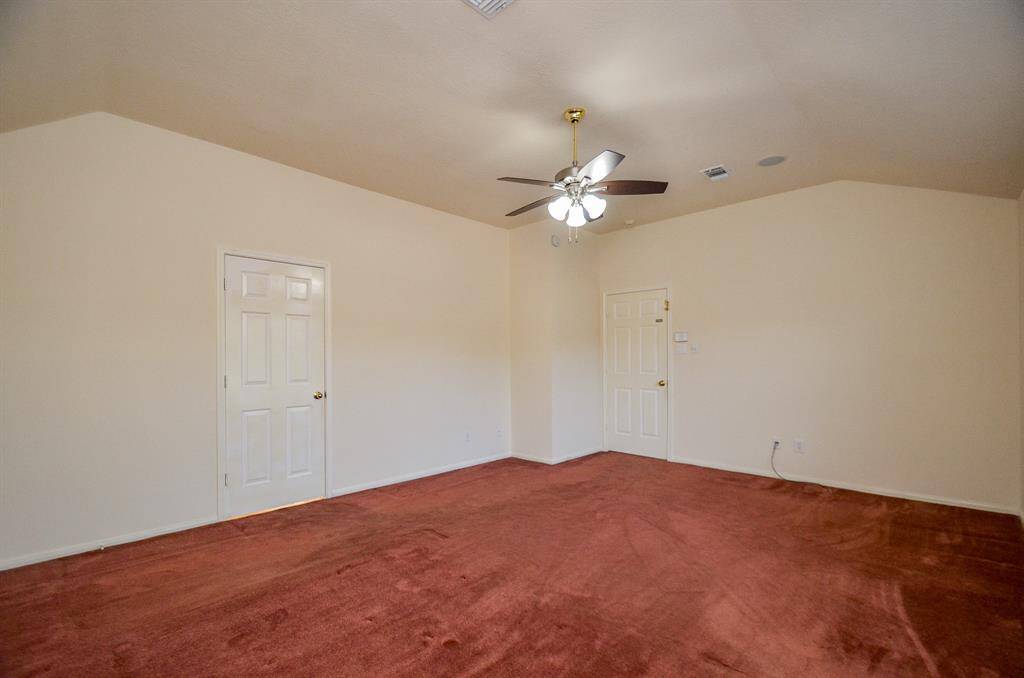 Another view of the spacious Primary bedroom with vaulted ceiling, neutral walls, and reddish carpet. Features a ceiling fan and two doors for convenient access.