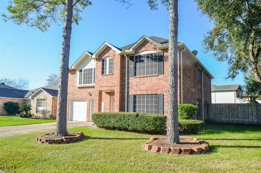 This is a charming two-story brick home with large windows and a well-maintained lawn. It features a two-car garage, mature trees, and a fenced backyard, perfect for privacy and outdoor enjoyment.