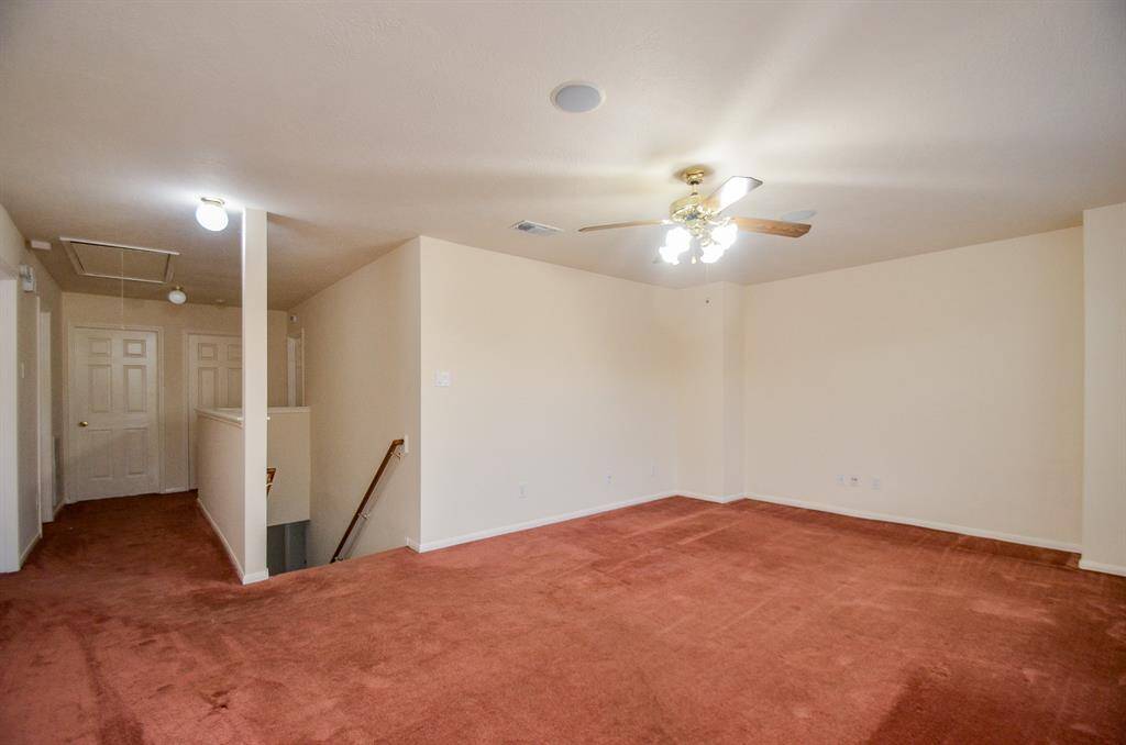This spacious Gameroom on the second floor features warm carpet flooring and neutral walls, offering a blank canvas for personalization. It includes a ceiling fan for comfort and a hallway leading to additional rooms, with access to a stairway. Perfect for a cozy living area or versatile family space.