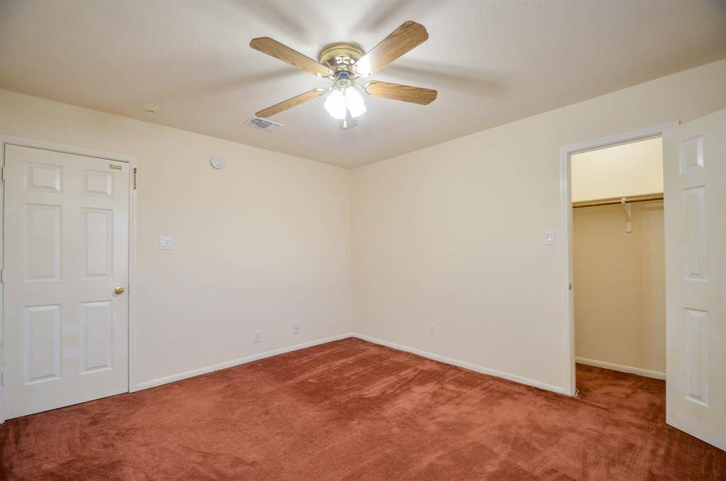 This is a cozy bedroom upstairs with soft beige walls, a ceiling fan, and rust-colored carpet. It features a walk-in closet and simple white doors.