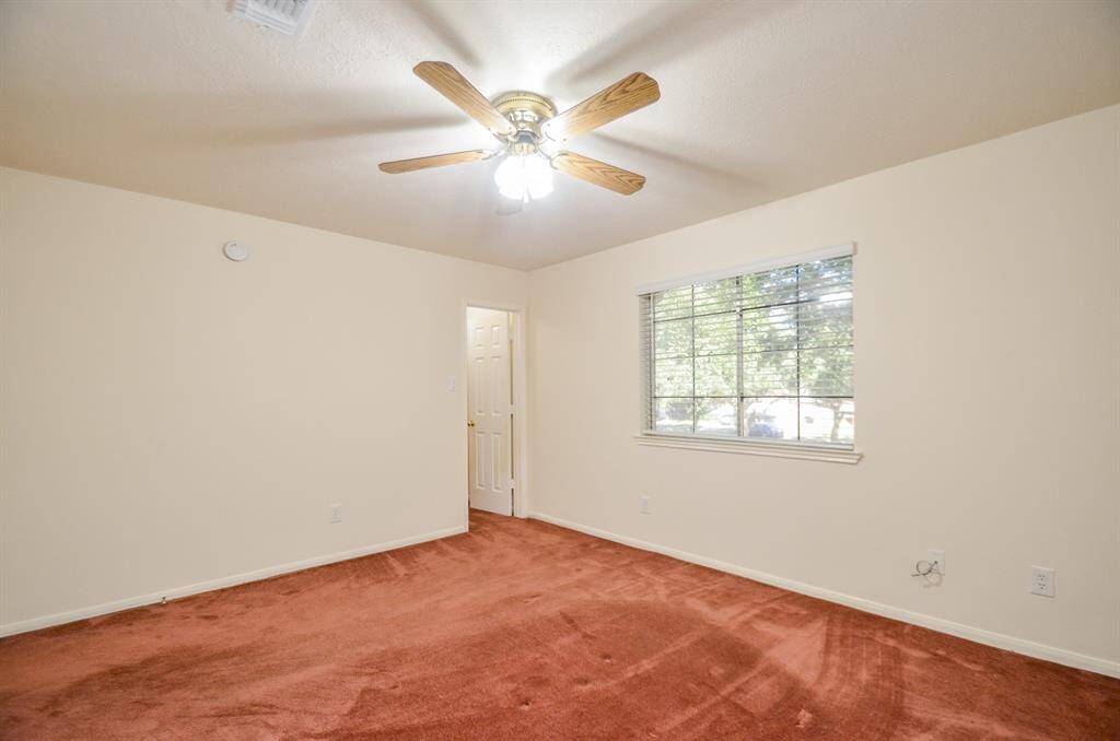 This bedroom upstairs features a cozy atmosphere with beige walls and a ceiling fan. It has a large window allowing natural light and is carpeted in a warm reddish-brown.