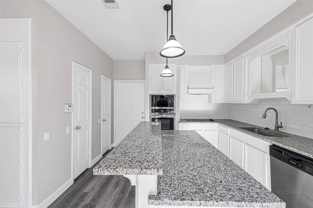 Modern kitchen with granite countertops, white cabinetry, stainless steel appliances, and pendant lighting. Features a spacious island and a sleek, clean design.