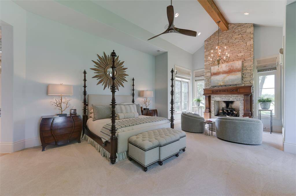 The elegant PRIMARY BEDROOM SUITE (22 X 18) is just off the formal Living Room and includes carpeted flooring, 16 foot pitched ceiling with exposed wood beam/recessed lighting/built-in speakers/ceiling fan, windows with auto-controlled drapery, softly painted walls and adjacent SITTING AREA (12 X 8) with its carpeted flooring, glass/metal hanging chandelier, gas log fireplace with slate stone surround/decorative carved wood mantel.
