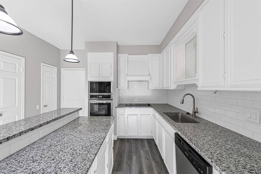 This kitchen features sleek granite countertops, white cabinetry, and modern stainless steel appliances. It has a stylish tile backsplash and pendant lighting, offering a bright and contemporary space.