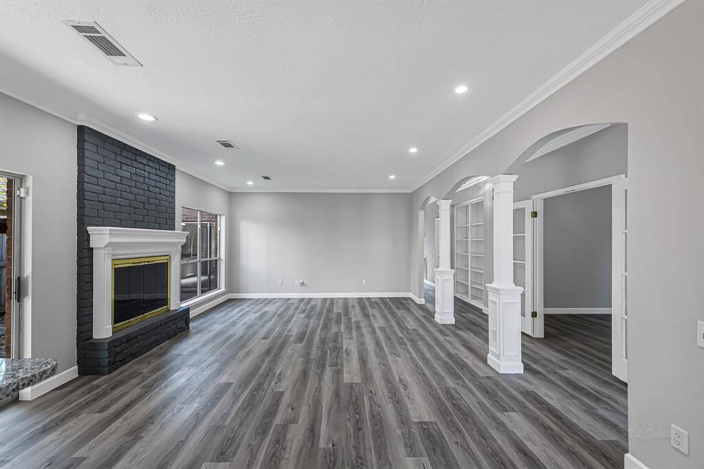 This spacious living room features modern gray flooring, a stylish dark brick fireplace, ample natural light, and elegant built-in bookshelves. Perfect for entertaining and cozy nights in.