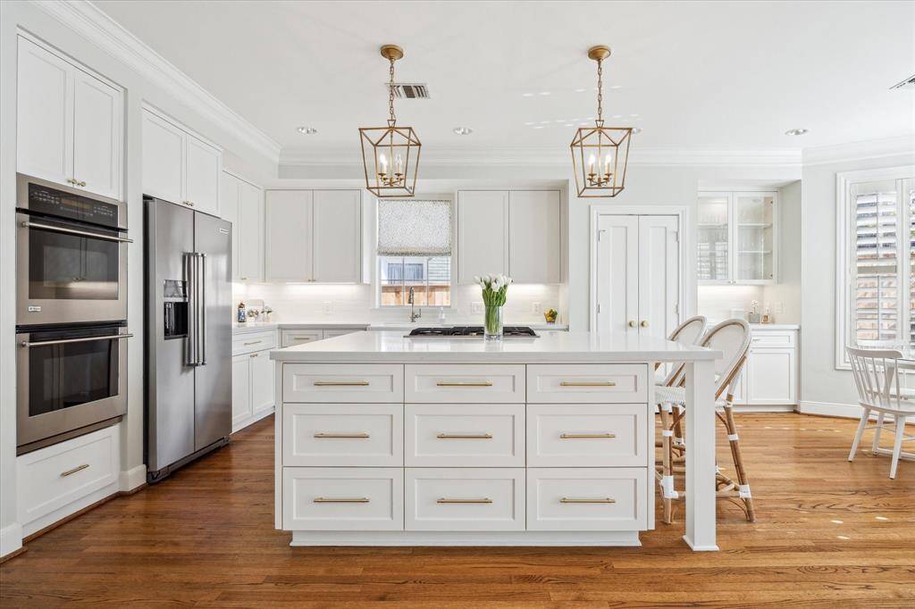 Straight-on view of large kitchen island, stainless double ovens and refrigerator/freezer.