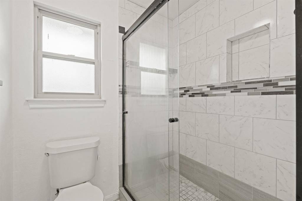 The primary walk-in shower has tile surround and a sliding glass door.