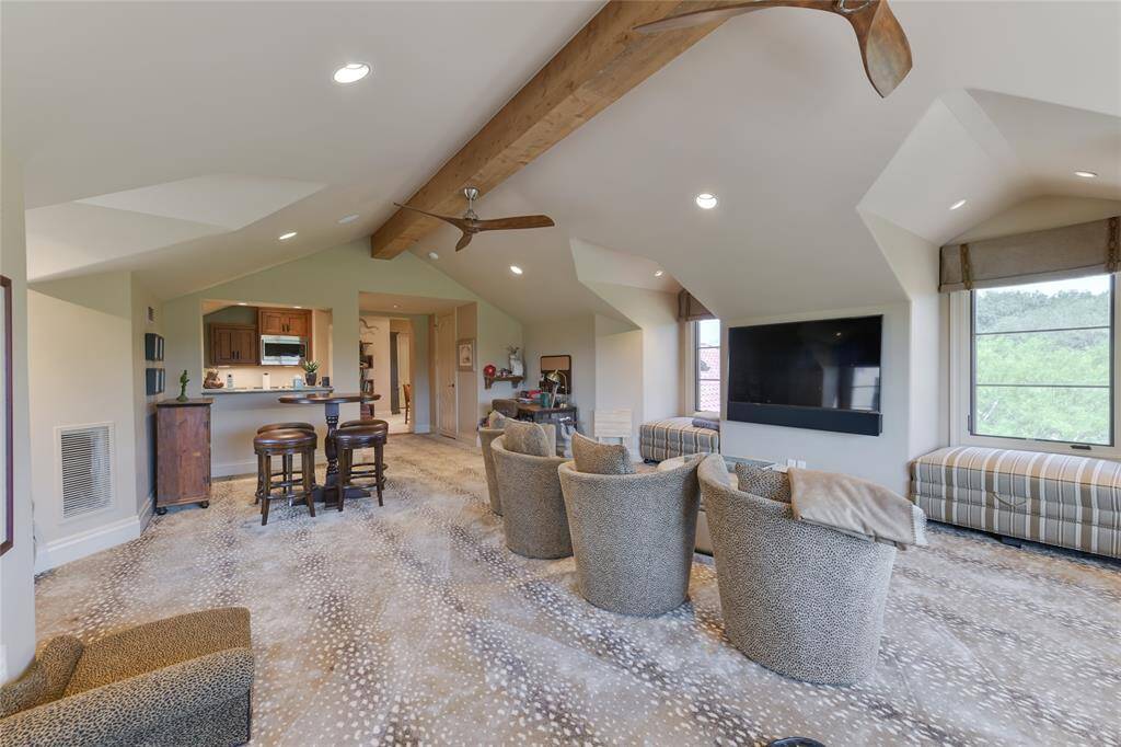 A conveniently located 2nd floor GAME ROOM (27 X 24) with its carpeted flooring, pitched ceiling with exposed wood beam/ceiling fans/recessed lighting/built-in speakers, dormer windows with built-in window benches (storage underneath), windows with Roman shades, two notable "big horn" light sconces, electronics closet and fully equipped WET BAR (marble counter/backsplash, bar seating, sink, wood floating shelves, cabinet front Scotsman ice maker, GE cabinet front mini refrigerator, stainless GE microwave).