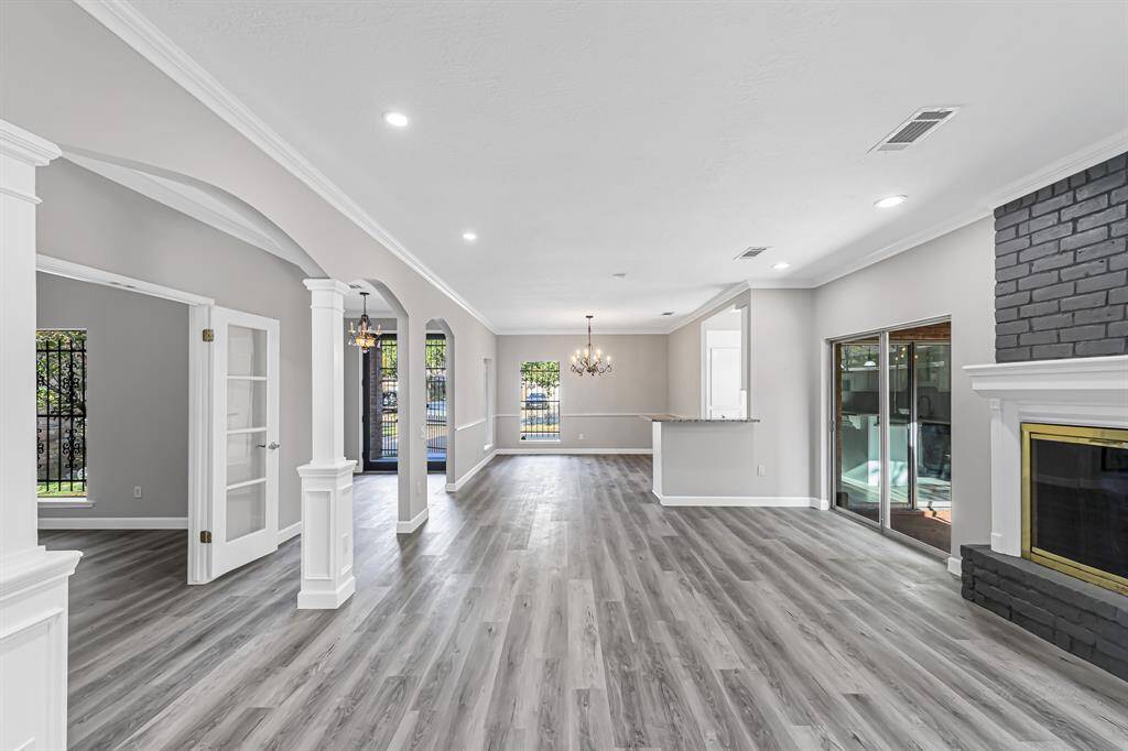 Spacious open-concept living area with modern gray flooring, a sleek dark painted fireplace, and abundant natural light. Features elegant archways, a chandelier, and sliding glass doors leading to an outdoor space. Ideal for entertaining and family living.