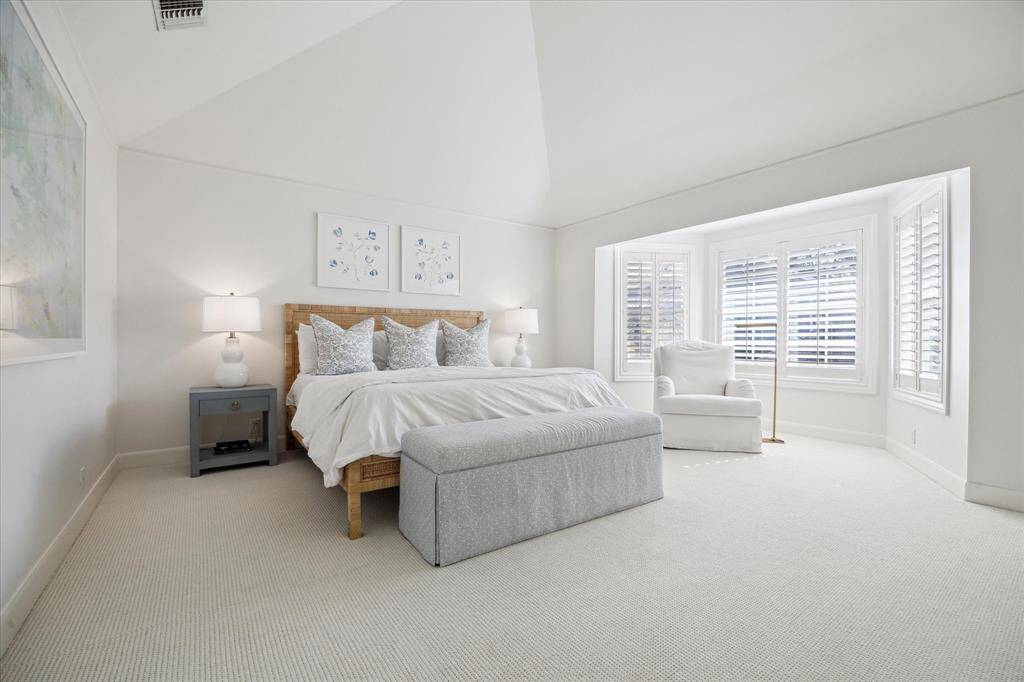 Spacious primary bedroom with high ceiling and sunny sitting area.