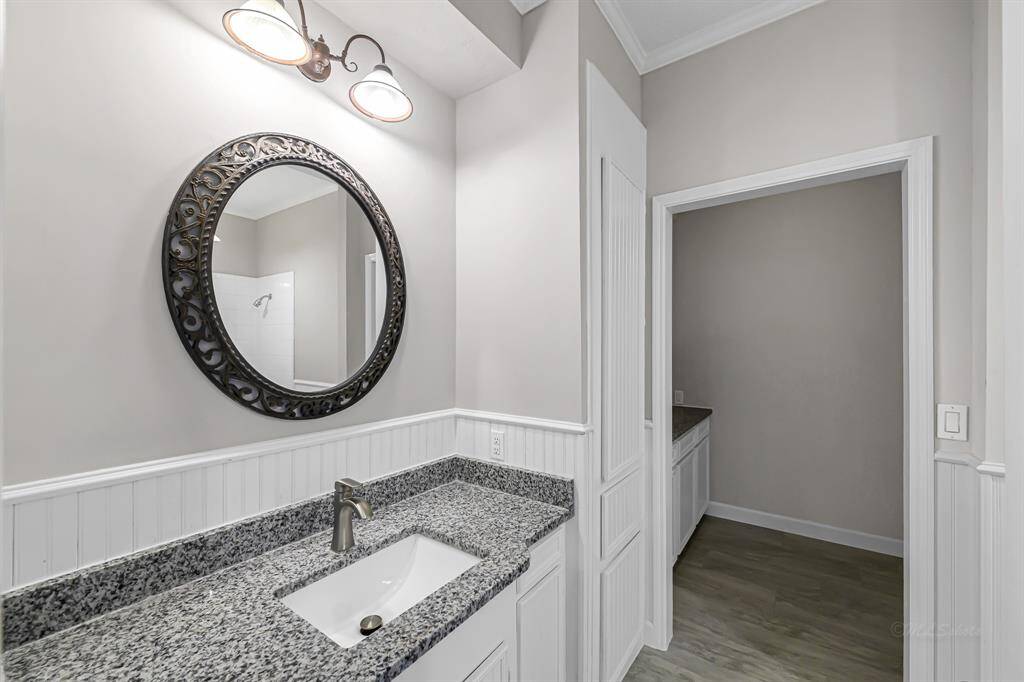 This photo showcases a modern bathroom with a granite countertop, elegant round mirror, and stylish light fixture. The space features wainscoting and neutral colors, creating a clean and inviting atmosphere.