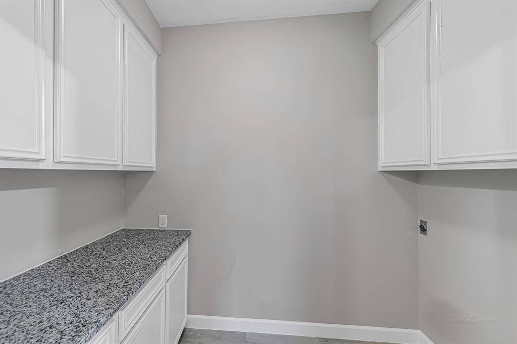 This photo shows a utility room with ample white cabinetry and a speckled granite countertop, offering plenty of storage space. The neutral wall color complements the modern design.