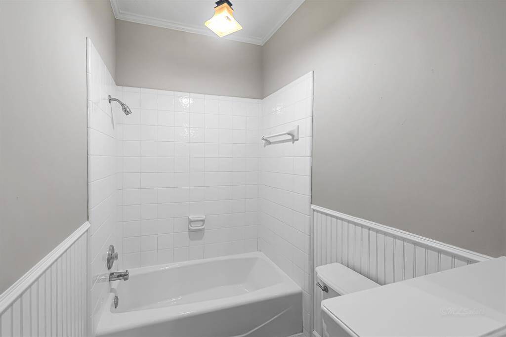 This bathroom features a clean design with white tiled walls, a bathtub and shower combination, and wainscoting for added style.