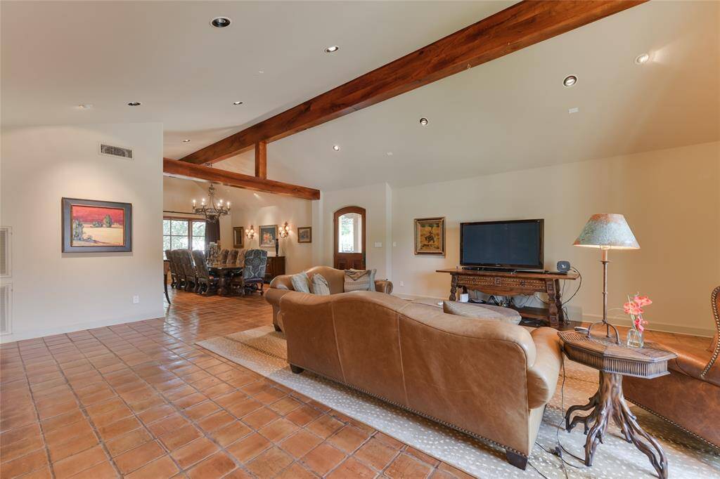 Upon entry through a stately wood/glass front door, the GUEST HOUSE'S LIVING ROOM (21 X 22) features saltillo tile flooring, pitched ceiling with exposed wood beams, gas log fireplace with metal screen/wood mantle, painted walls, mullioned windows with drapery, recessed lighting/art lighting, built-in shelving with cabinets below. Notice the DINING ROOM beyond (19 X 14) with its metal/glass chandelier.