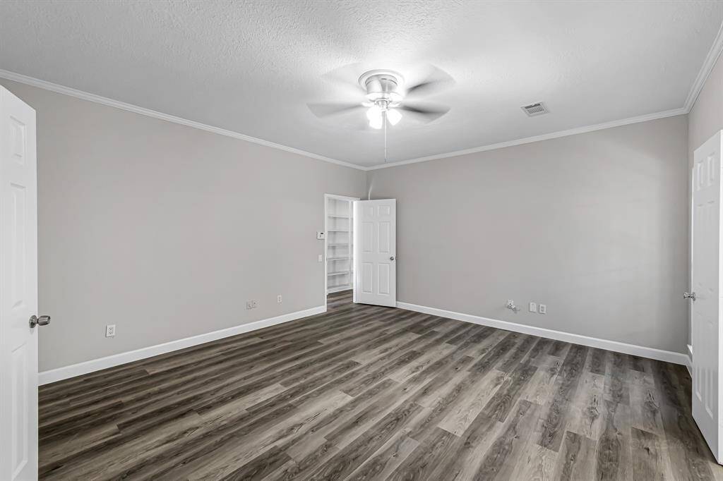 This room features a neutral color palette with light gray walls and wood-look flooring. It includes a ceiling fan, multiple doors, and ample natural light, offering a spacious and versatile area.