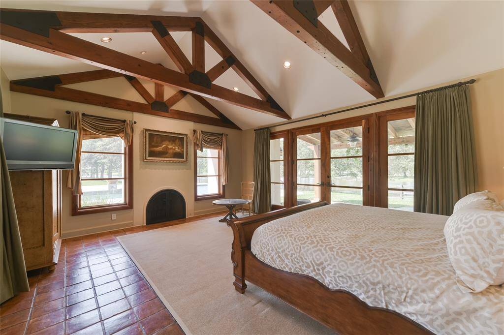 Sophisticated elegance describes the Guest House's PRIMARY BEDROOM (20 X 16) with its Saltillo tile, painted walls, central gas fireplace with metal arched screen, pitched ceiling with exposed wood beam supports, wood framed glass doors opening to back patio overlooking the lake, cedar walk-in closet, walk-in closet with built-in drawers/cabinets, en suite bath with spa tub/glass front walk-in shower/dual sinks/vanity seating/private water closet/linen storage.