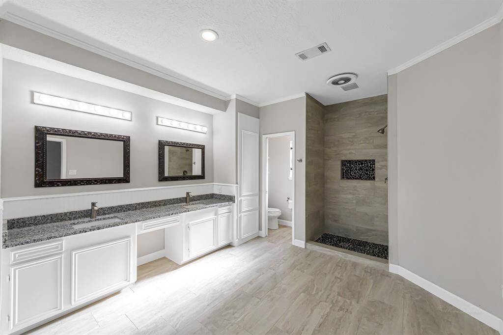Spacious modern bathroom with double vanity, granite countertops, and large mirrors. Features a walk-in shower with stylish tile accents and a separate toilet area for added privacy.