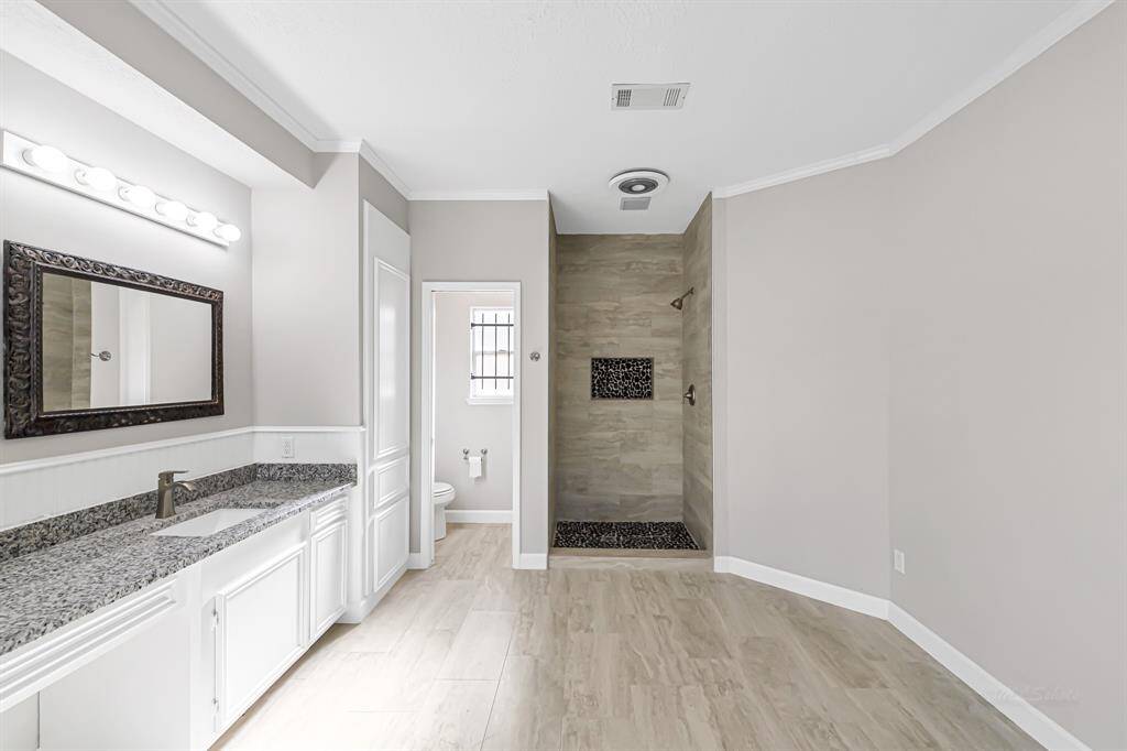 This photo showcases a modern bathroom with a spacious walk-in shower featuring pebble flooring and a built-in shelf. The space includes a sleek vanity with granite countertops and ample lighting, creating a bright and elegant atmosphere.