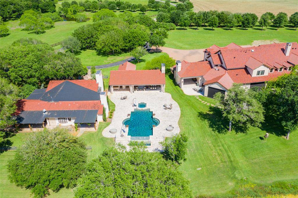 View of the guest and main houses situated on both sides of the complex's heated/over-sized pool with infinity edge/water features/hot tub, fire pit and covered outdoor kitchen and dining areas - all surrounded by open pasture areas with native Pecan/Mixed Oak/Mesquite trees!
