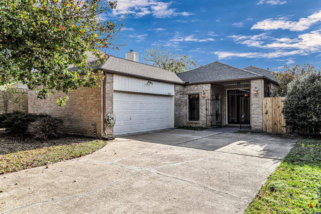 This charming single-story home features a classic brick exterior, a spacious two-car garage, and a welcoming entrance with wrought iron details. The front yard is well-maintained with mature trees, and a fenced side area adds privacy.