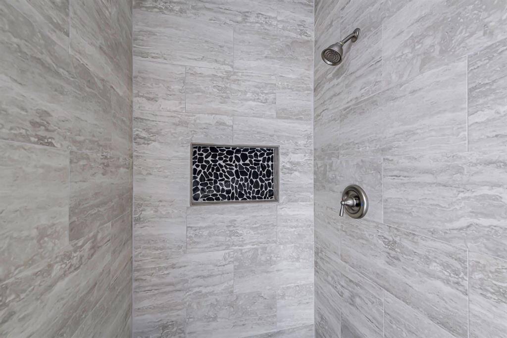 This photo showcases a modern shower with sleek gray marble tiles and a stylish pebble-tiled niche for storage. The fixtures are contemporary and metallic, adding a touch of elegance to the space.