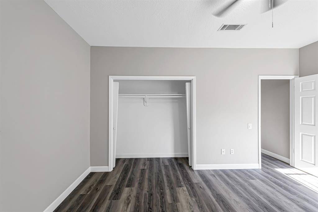 This room features modern gray walls, sleek wood-style flooring, and a spacious closet with sliding doors. It offers a clean and bright atmosphere, perfect for a bedroom or home office.