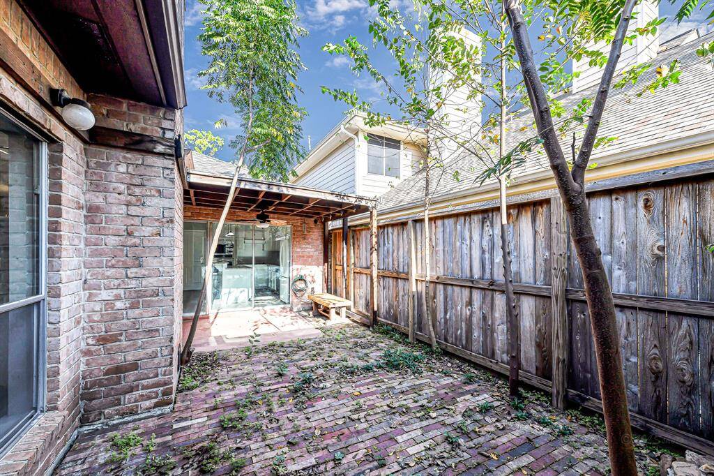 This photo showcases a cozy brick patio area with a wooden fence, partially covered by a covered patio. The space has some trees and plants, offering the potential for a charming outdoor retreat.