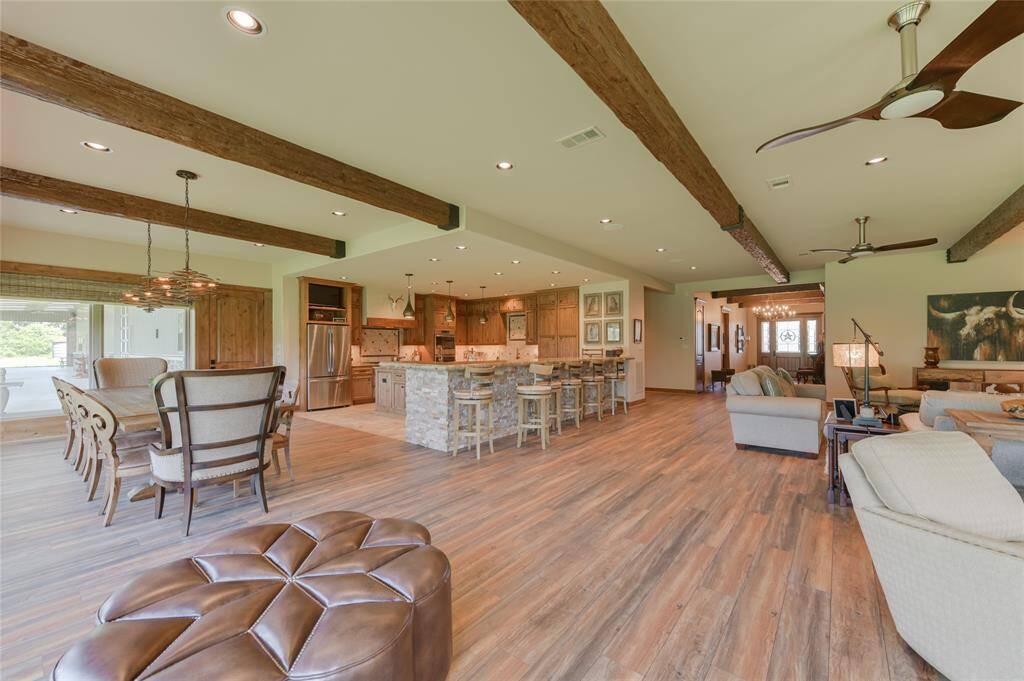 View of the open floor plan from the LIVING ROOM facing toward the DINING AREA (19 X 14) and nearby KITCHEN (19 X 19). The Dining Room includes the same hardwood flooring, exposed beams and windowed area as the Living Room. The Kitchen features tile flooring, center island, wet bar with hammered copper sink, breakfast bar seating, stone counters, stained wood cabinets/drawers, 2 stainless sinks, stainless Zephyr/GE/Dacor/Scottsman appliances - everything needed for the visiting chef!