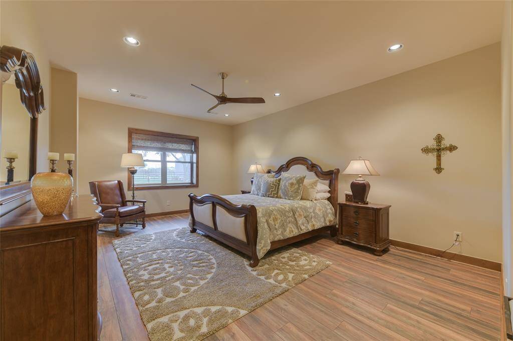 One of two GUEST BEDROOMS on the Barndominium's first floor - this one (34 X 15) features hardwood flooring, 2 dual fold closets with shelving, window with shades, recessed lighting, ceiling fan and en suite bath (granite counter/tile flooring/wood framed mirror/dual sinks with cabinets below/walk-in frame-less glass shower with tile surround/light sconces.