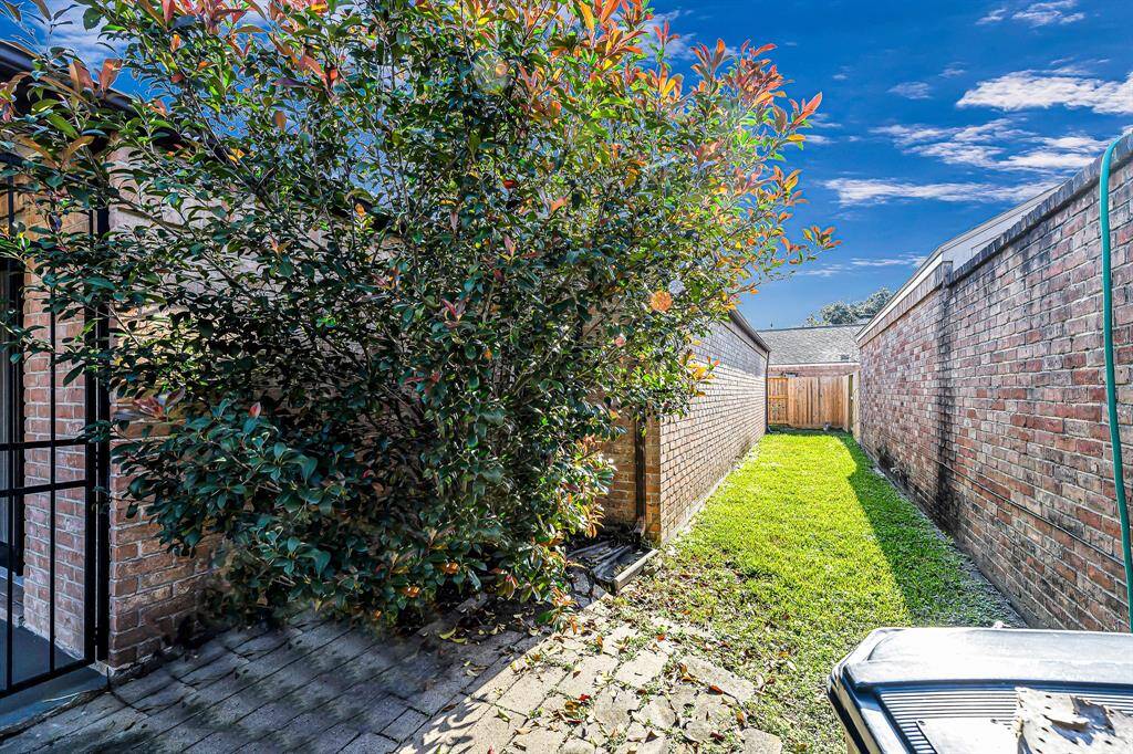 A narrow side yard features a small grassy area bordered by brick walls, with a leafy tree adding greenery. The space is enclosed and includes a paved section for easy access.