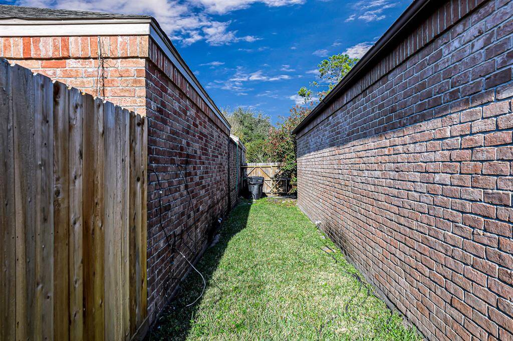 This photo shows a narrow side yard with a grass strip between two brick walls and a wooden fence on the left. It's a low-maintenance space, ideal for storage or a small garden area.