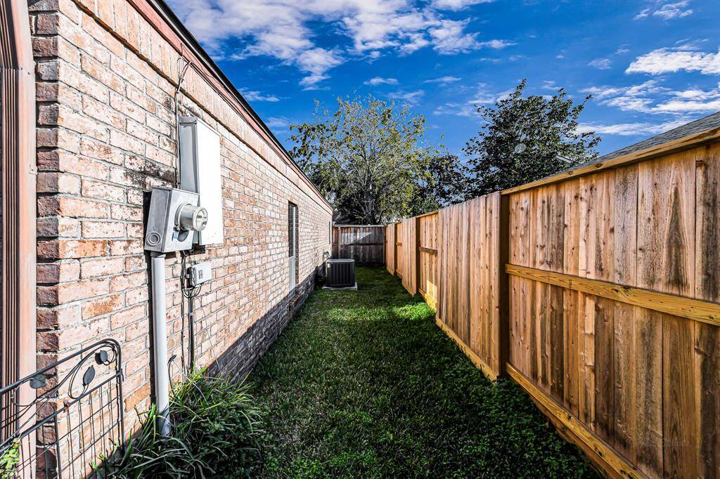 This photo showcases a narrow side yard with a brick exterior wall on one side and a wooden privacy fence on the other. The area is grassy, providing a small green space, with an air conditioning unit visible near the back.