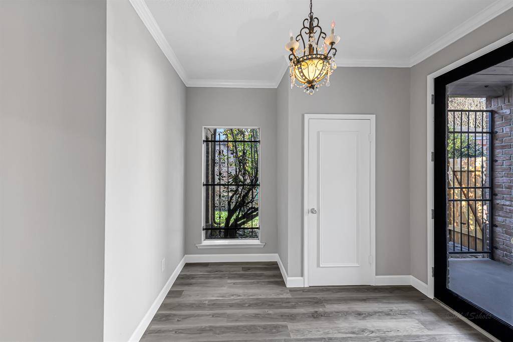 This room features elegant hardwood flooring, a decorative chandelier, and a window with wrought iron detailing. There's also a door leading to the front patio space, providing natural light and a touch of charm.
