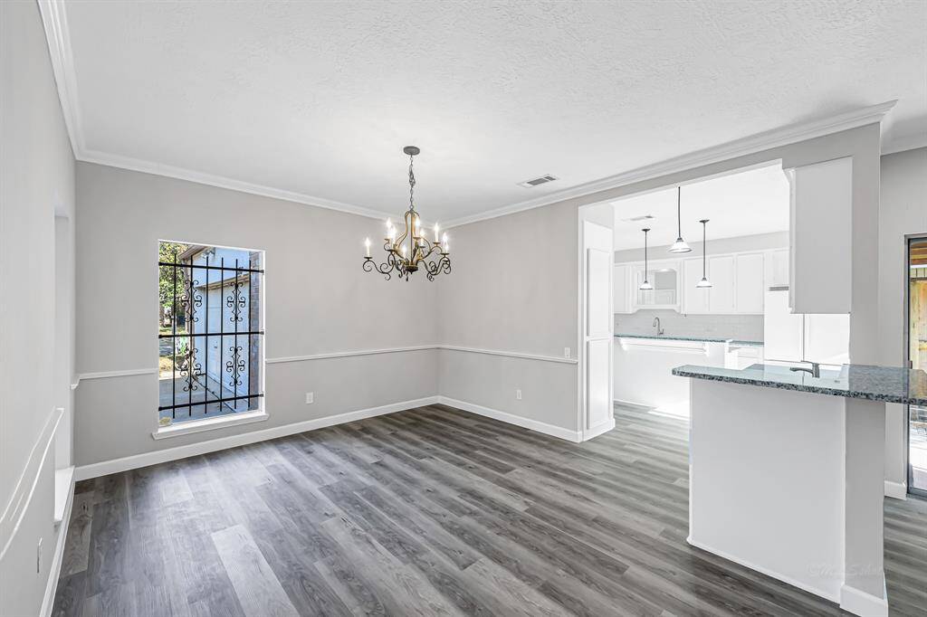 This photo showcases a bright, open dining area with elegant gray flooring and a classic chandelier. It seamlessly connects to a modern kitchen with white cabinetry and granite countertops, creating a welcoming space for family gatherings.