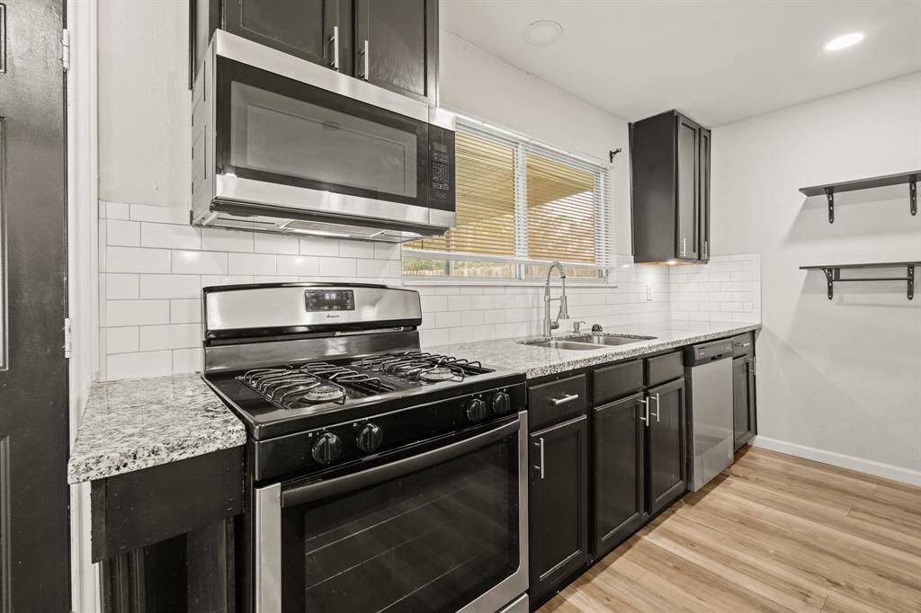 The kitchen features black cabinets, white tile backsplash, and stainless steel appliances creating a clean and timelessaesthetic.