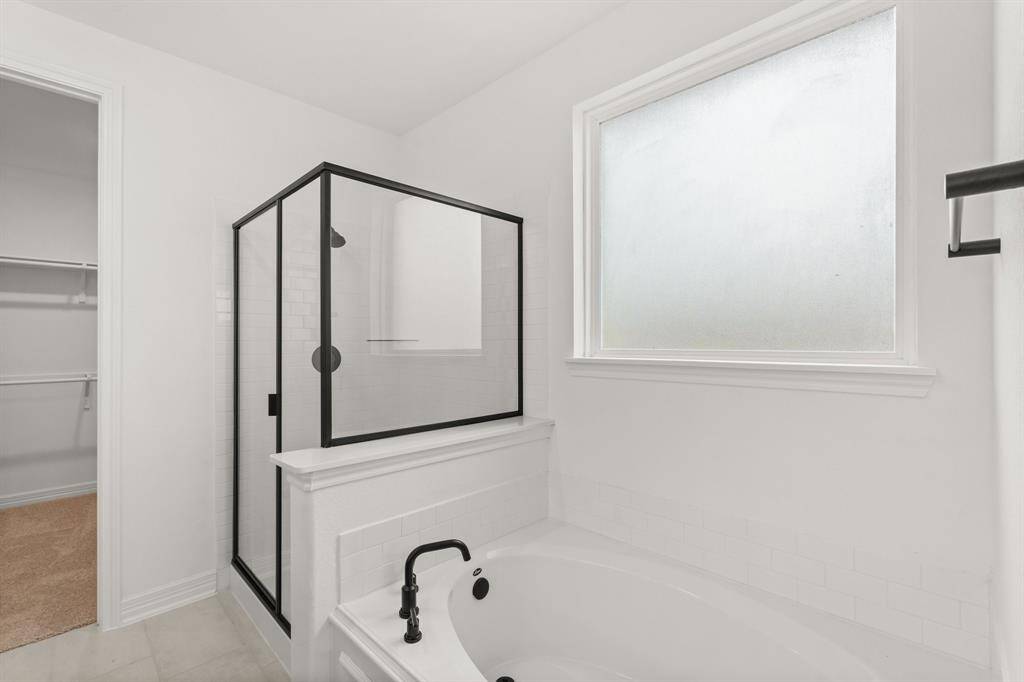 This additional view of your primary bathroom features tile flooring, fresh paint, walk-in shower, a separate garden tub, and a large walk-in closet.