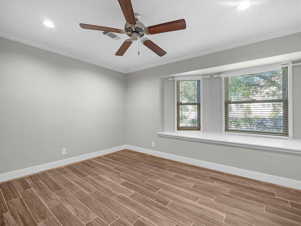 The second bedroom boasts elegant handscraped wood-look porcelain tile floors, a cozy window seat, and stylish recessed lighting. It features crown molding, a ceiling fan, fresh grey paint with white trim, faux wood blinds, and extended baseboards. Ample storage includes a wall of built-in shelves and two wardrobe closets.