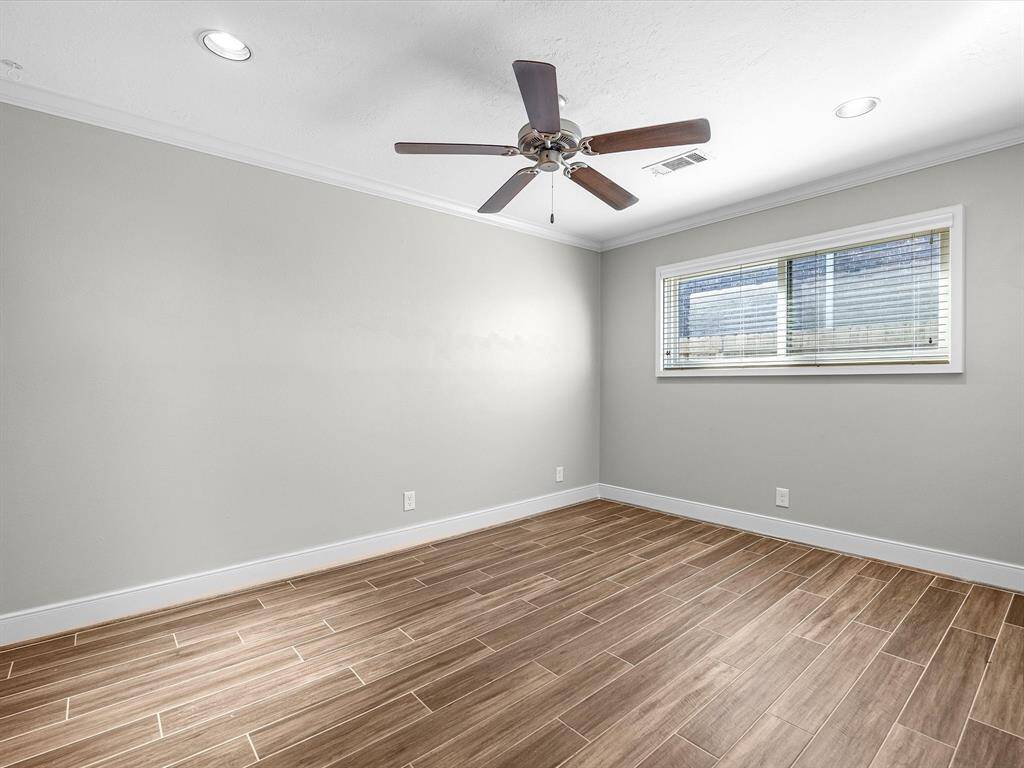 The third bedroom features elegant wood-look porcelain tile, recessed lighting, crown molding, a ceiling fan, and fresh grey paint with white trim. Enjoy ample storage with a wardrobe closet and enhanced style with faux wood blinds and extended baseboards.