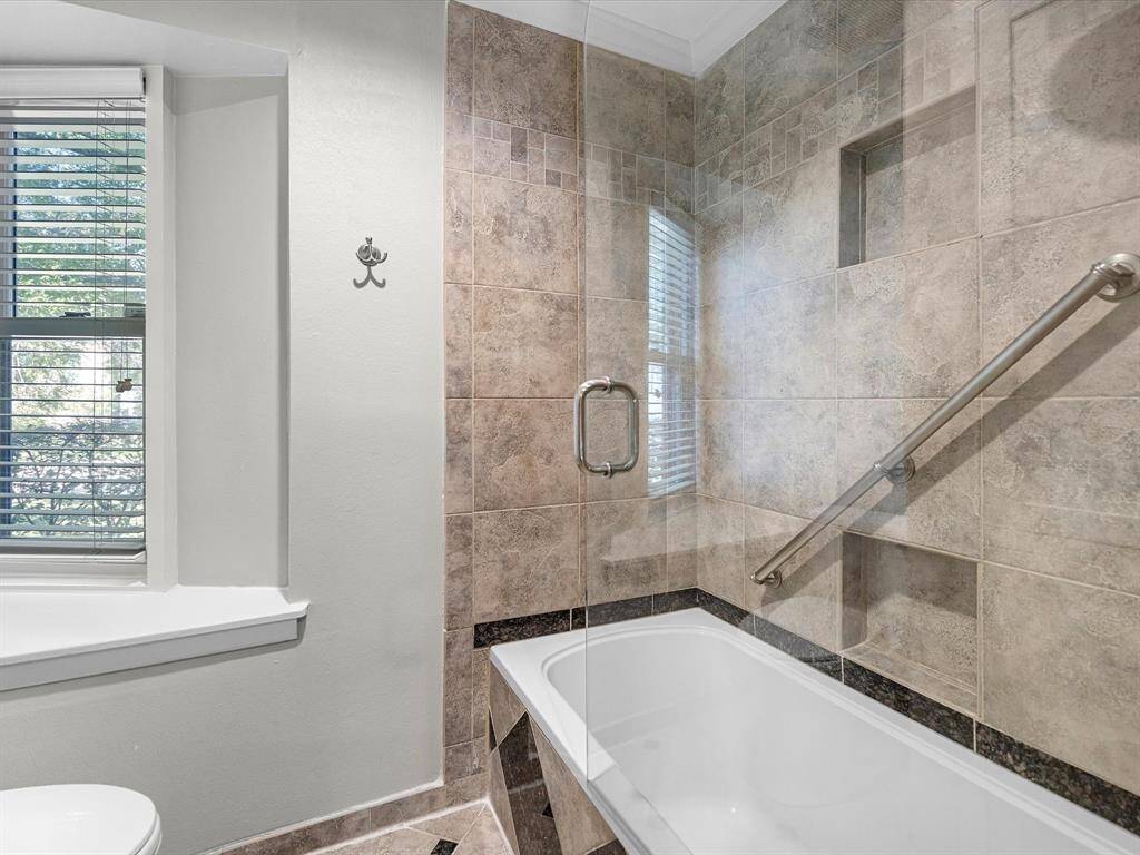 This elegant secondary bathroom features a modern shower-tub combo with stylish tile and a glass door. Enjoy natural light and added safety with a convenient grab bar.