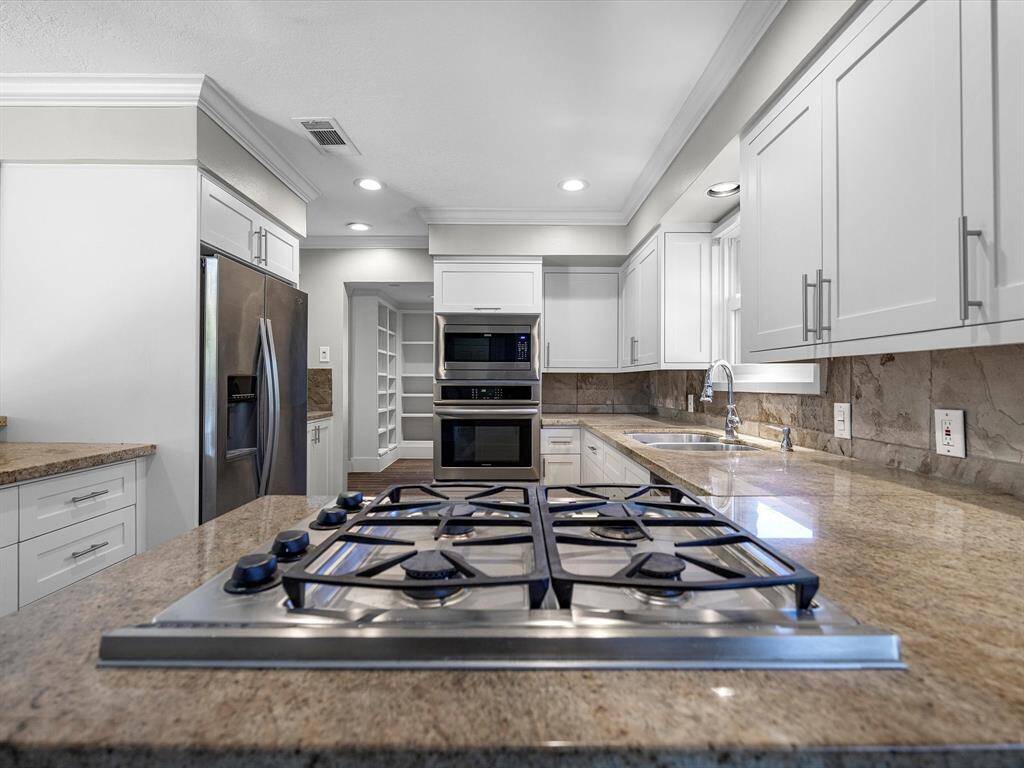 Cook with ease on the sleek Dacor 4-burner gas range in a kitchen featuring recessed lighting, elegant crown molding, and fresh grey paint with crisp white trim.