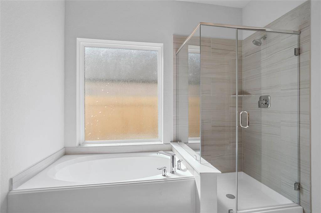 Another view of the primary bathroom which features a large walk-in shower with tile surround, garden tub to soak after a long hard day, large window allowing in the natural light, custom paint, sleek and dark modern finishes.