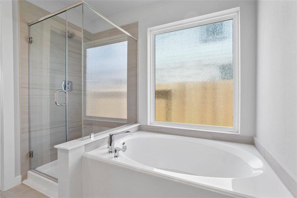 Additional view of the primary bathroom features a dark framed walk-in shower with tile surround, separate garden tub for soaking after a long day, and gorgeous tempered glass windows to allow in the natural light!