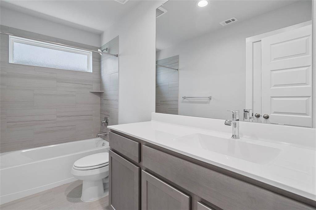 Secondary bath features tile flooring, bath/shower combo with tile surround, stained wood cabinets, beautiful light countertops, mirror, dark, sleek fixtures and modern finishes!