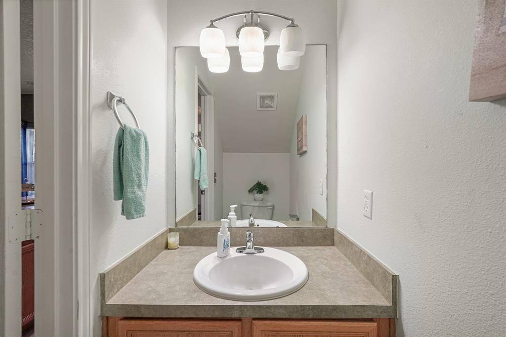 This bathroom features a clean, modern design with a single sink vanity, ample counter space, and a large mirror. The lighting is bright and inviting, complemented by light-colored walls and a simple, functional layout.